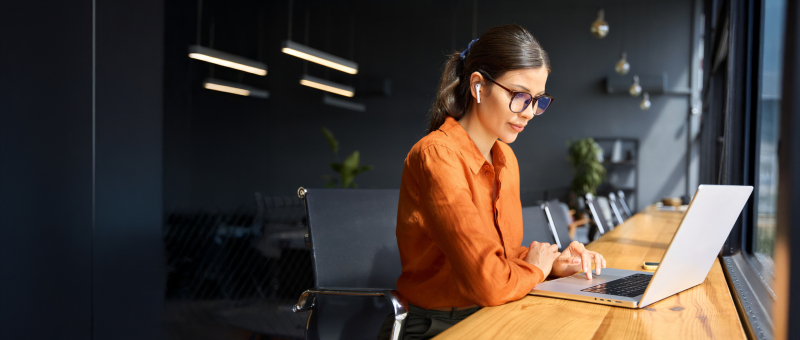 Latin hispanic young business woman working on laptop computer at office desk with city view. Indian entrepreneur manager businesswoman using pc for work, learning at workplace. Banner, copy space